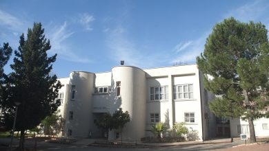 White two-storey building with rounded towers, signed Afife Jale Salonu, among pine trees under a blue sky