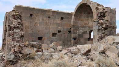 Ruined stone church with a vaulted apse and scattered rubble under a partly cloudy sky in Aksaray, Anatolia