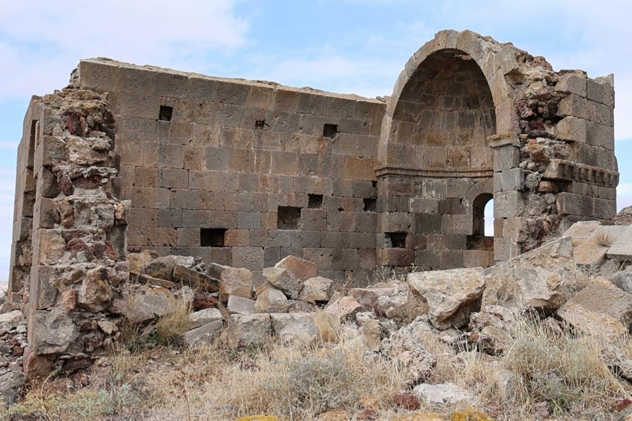 Ruined stone church with a vaulted apse and scattered rubble under a partly cloudy sky in Aksaray, Anatolia