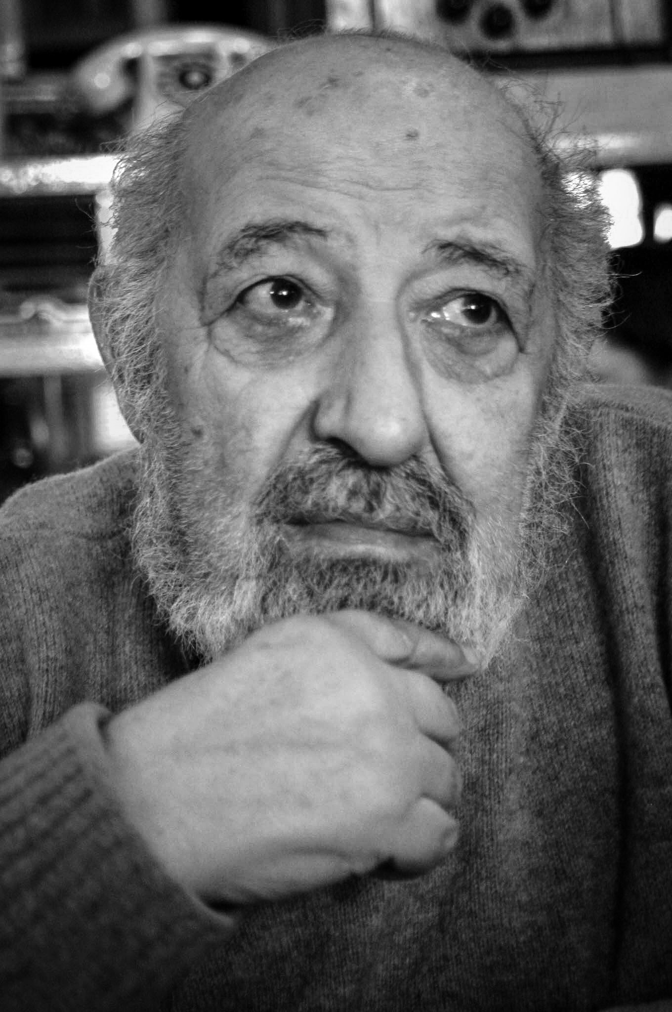 Black-and-white close-up portrait of an elderly bearded man in a wool sweater, resting his chin on his hand and looking aside.