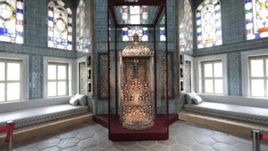 Ornate mother-of-pearl inlaid throne in a glass display case in a tiled chamber with stained-glass windows and cushioned benches