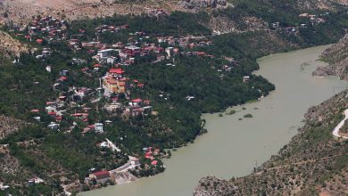 Aerial view of a hillside town with red-roofed houses beside a wide green river in a rocky mountain canyon