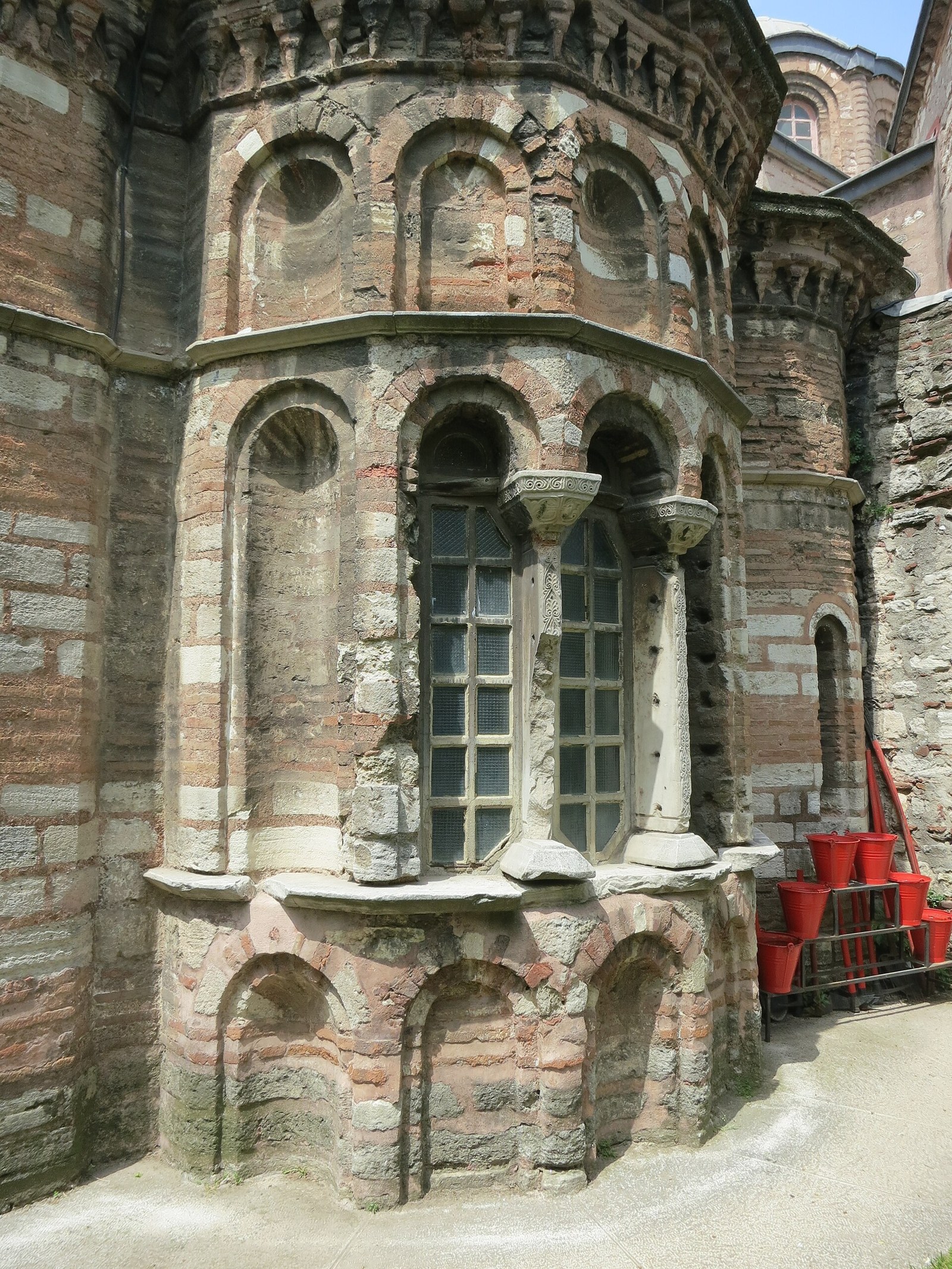 Brick and stone apse of an old Byzantine-style building in Istanbul, with arched windows and red fire buckets nearby