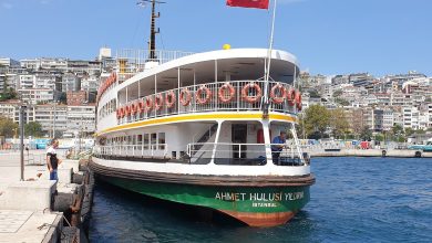 Istanbul ferry Ahmet Hulusi Yildirim moored at a Bosphorus pier, a Turkish flag flying and hillside buildings behind