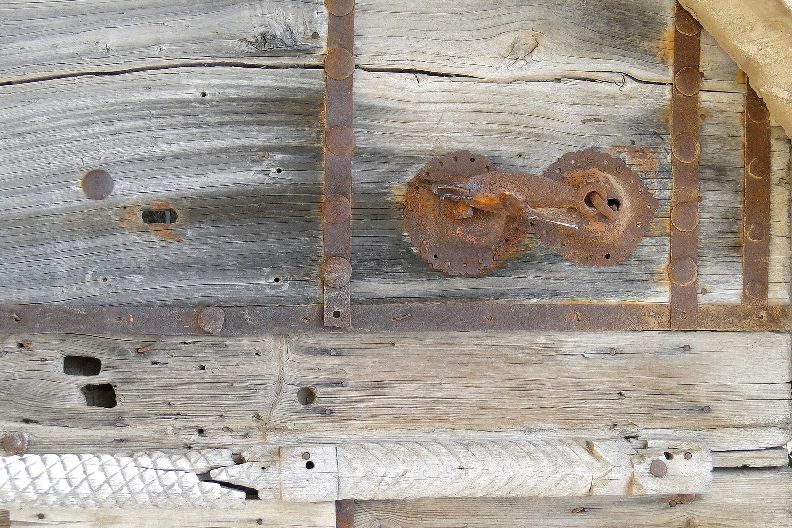 Close-up of an old wooden door with rusty iron hardware, including a decorative latch and studded bands.