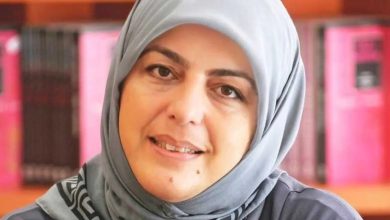Close-up portrait of a smiling woman in a gray headscarf in front of bookshelves