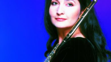 Studio portrait of a dark-haired woman in a black velvet top holding a flute against a deep blue background