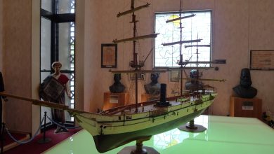 Model of a 19th-century sailing ship with steam funnel on a lit table in a museum, with busts and a mannequin in the background
