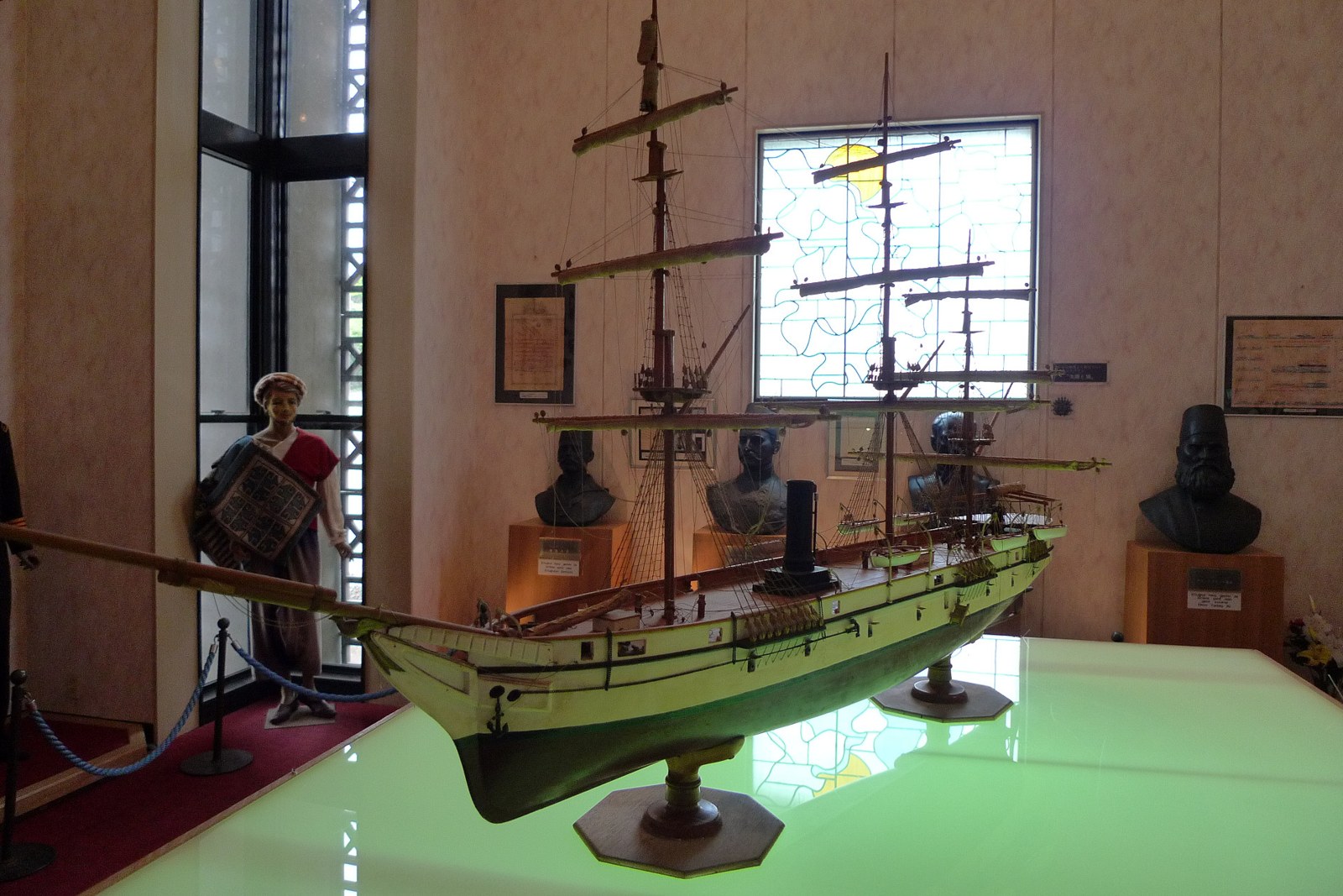 Model of a 19th-century sailing ship with steam funnel on a lit table in a museum, with busts and a mannequin in the background