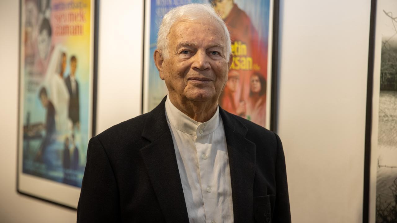 Portrait of Süleyman Saim Tekcan standing in front of framed posters.