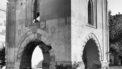 Black-and-white view of the stone mosque pavilion on arches in the courtyard of Sultanhanı Caravanserai, with paving and tree leaves.