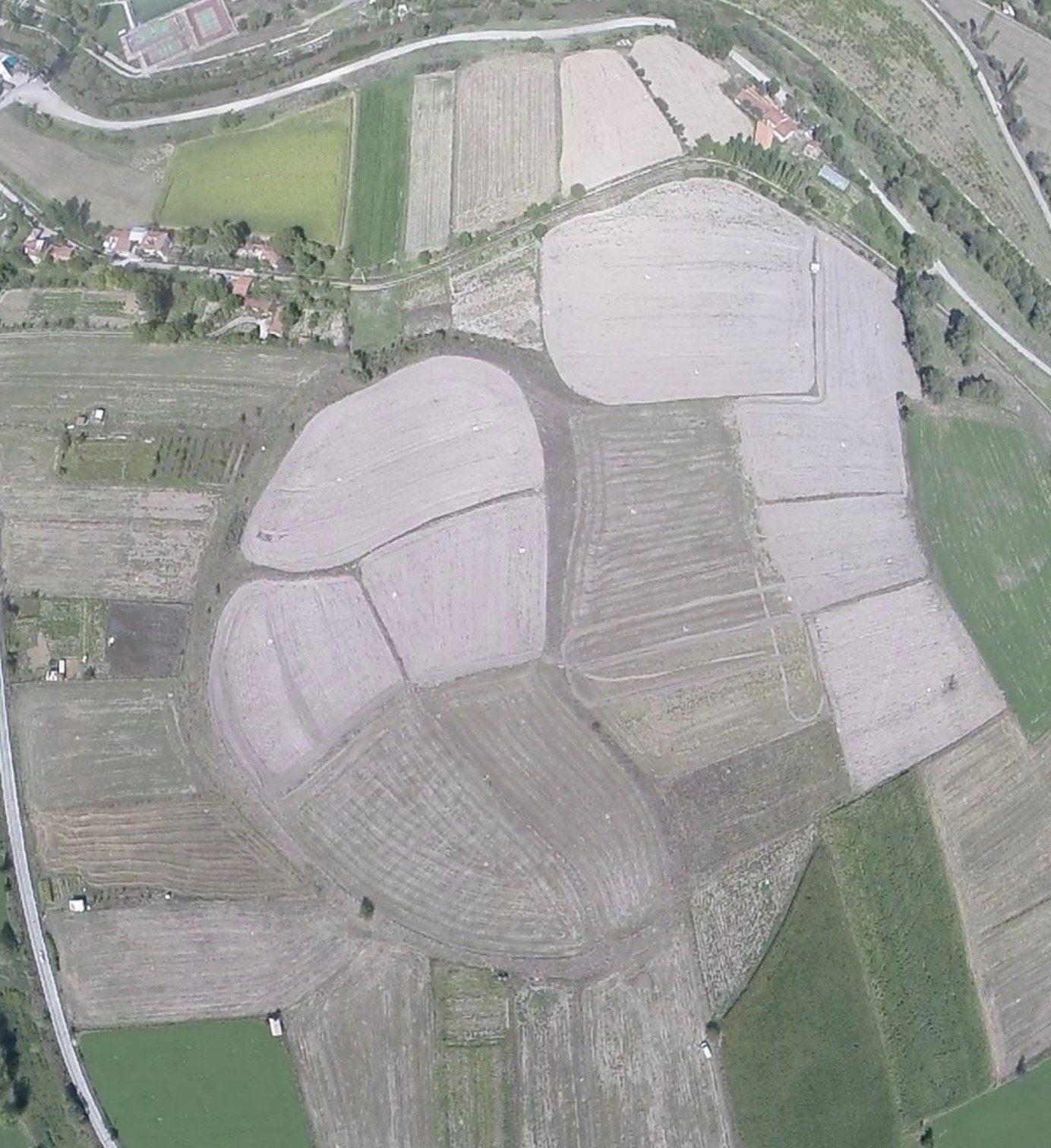 Aerial view of a rounded mound surrounded by plowed farm fields, roads and houses, apparently the Tavşanlı Höyük archaeological site