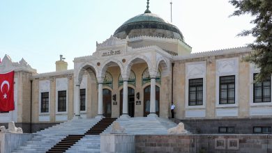 Ankara Ethnography Museum's marble entrance with arches and a green dome, a Turkish flag hanging at left and stone lions on the steps