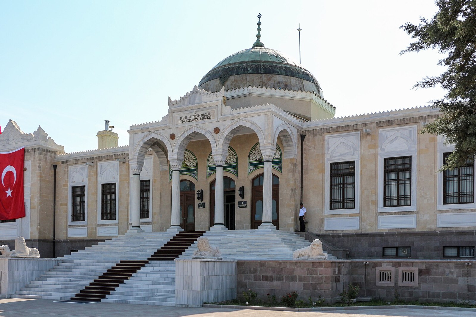 Ankara Ethnography Museum's marble entrance with arches and a green dome, a Turkish flag hanging at left and stone lions on the steps