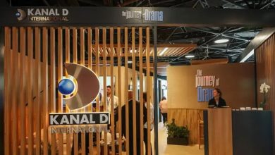 Kanal D International stand with wooden slats and 'The Journey of Drama' signs, with visitors and a staff member at a desk