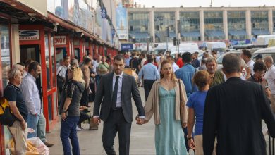 A man in a dark suit and a woman in a green dress hold hands as they walk along a crowded Istanbul street in what looks like a TV drama scene.