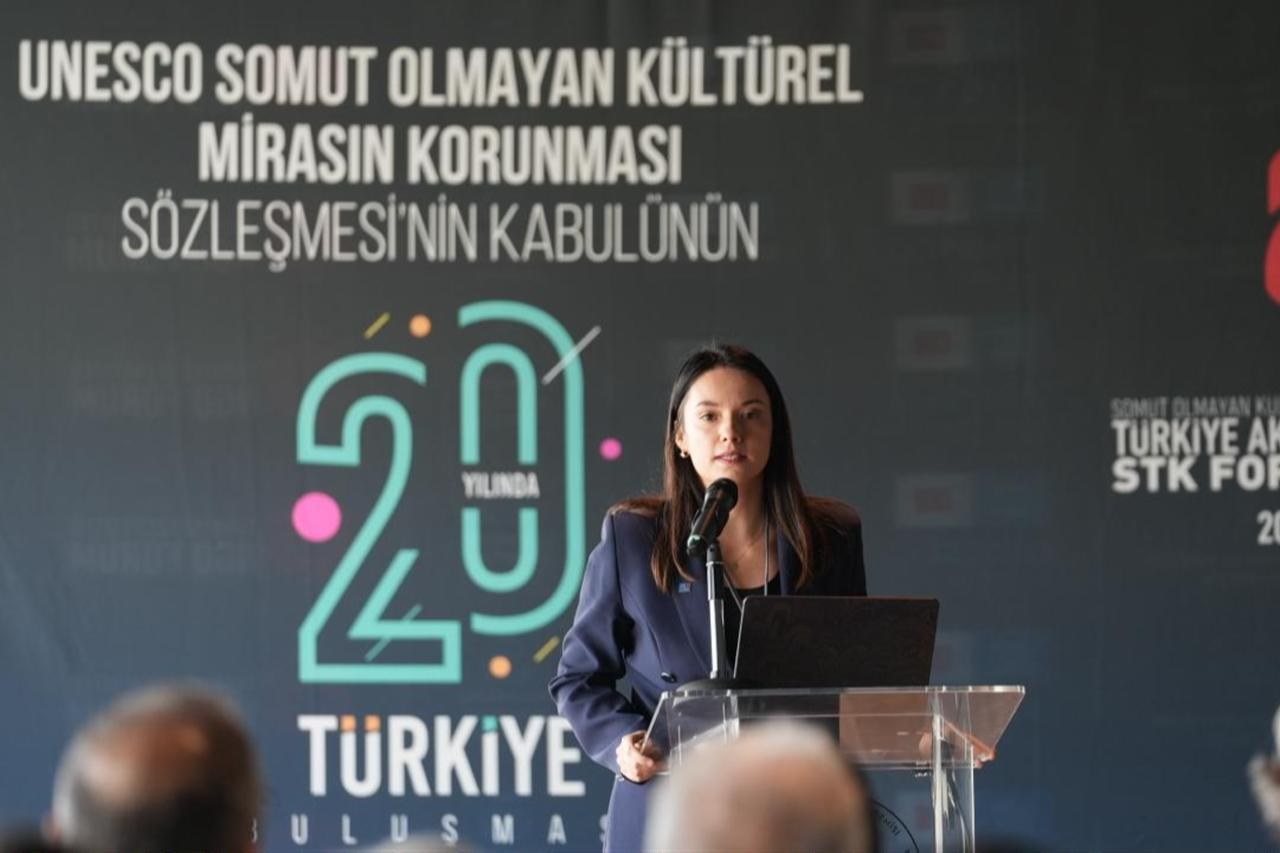 Woman in a navy blazer speaks at a podium before a backdrop marking 20 years of UNESCO's intangible heritage convention in Türkiye
